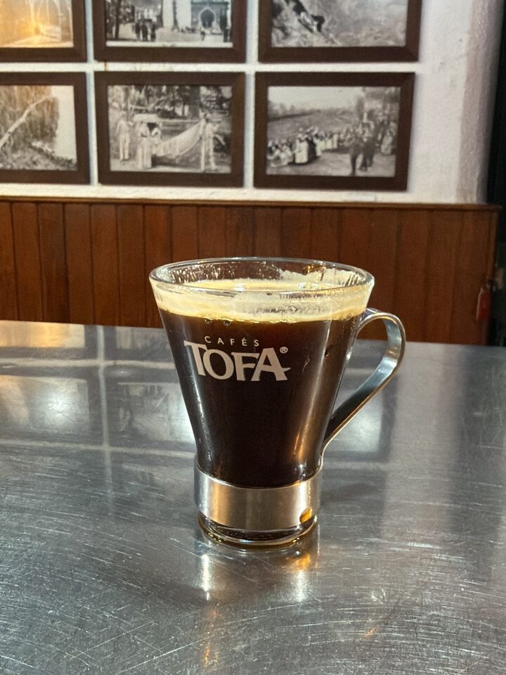 A glass of coffee on the bar counter, old photographs of the parish on the wall